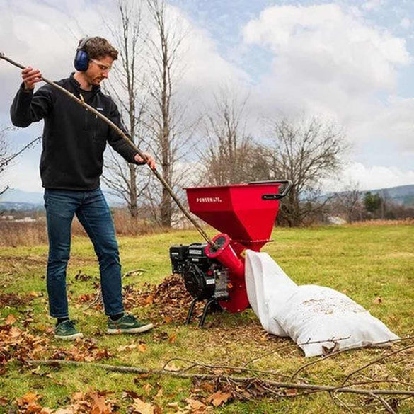 Person using a red tree chipper in an outdoor setting with trees and grass.